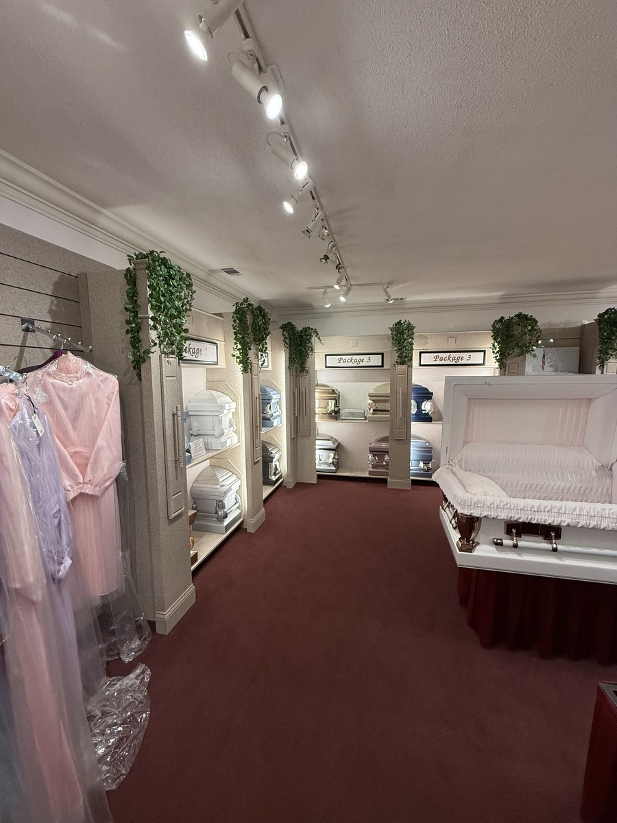 Interior of a bridal shop with dresses, veils, and display shelves on a burgundy carpet.