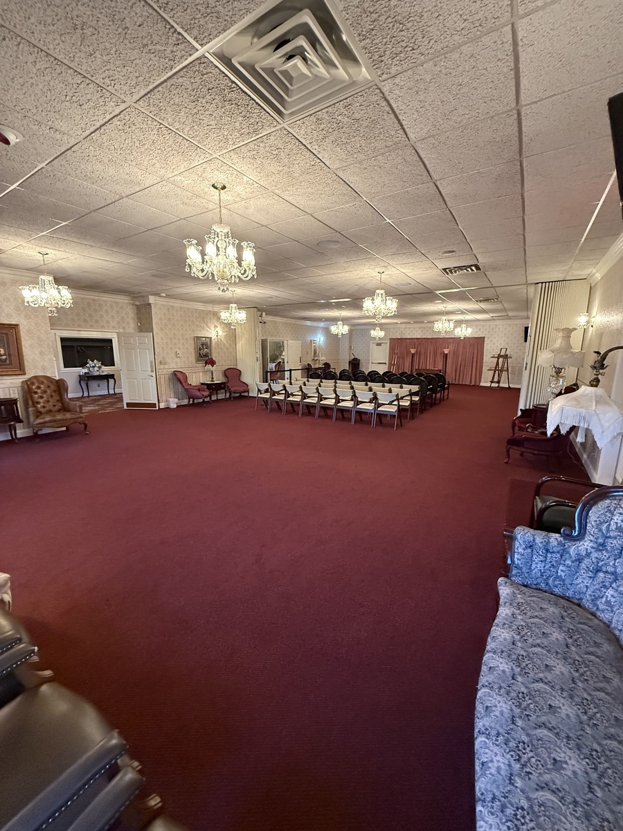 Spacious banquet hall with red carpet, chandeliers, rows of chairs, and white draped walls