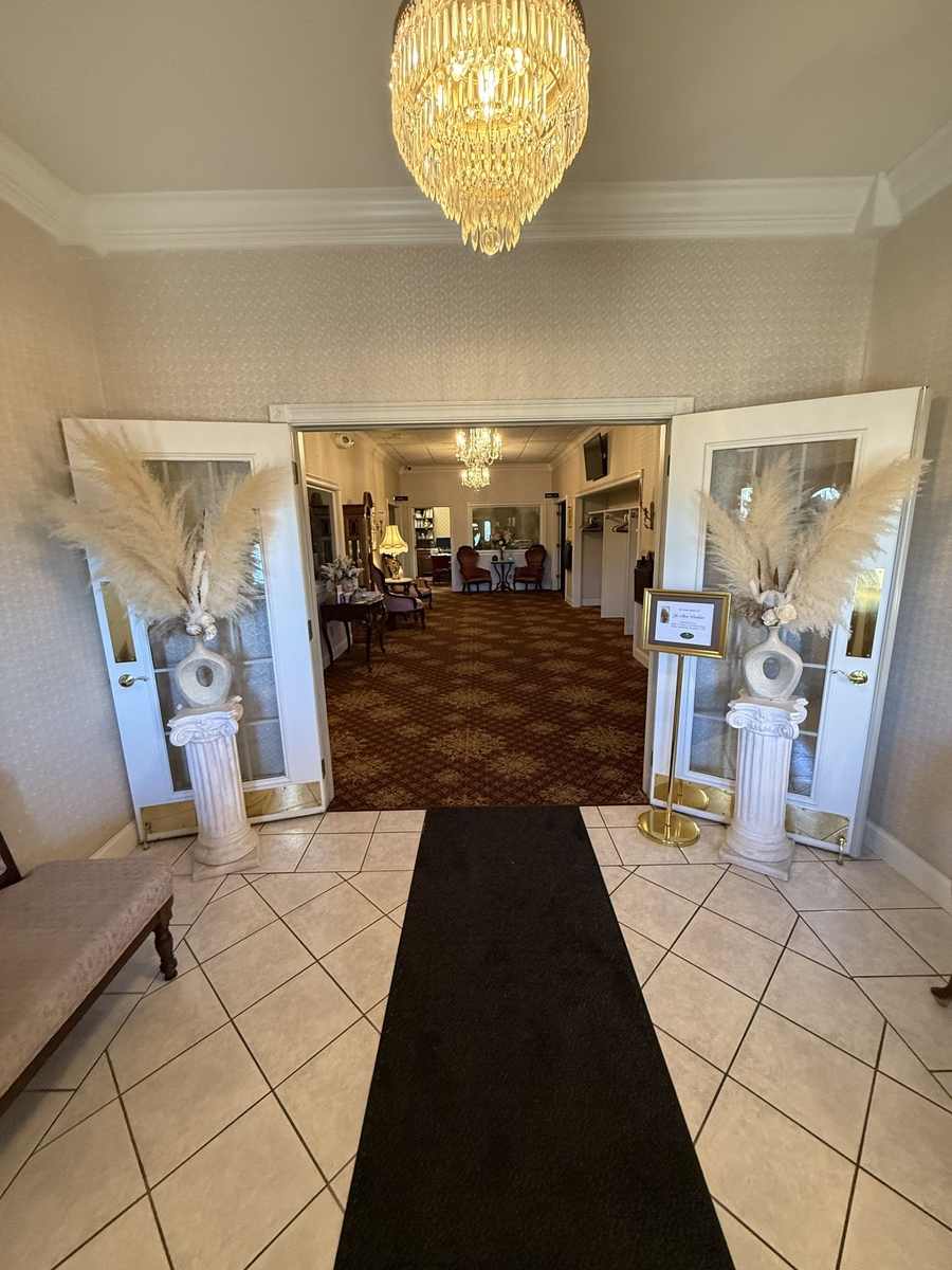 Elegant entrance hall with chandelier, tiled floor, black runner, and open double doors to a decorated room