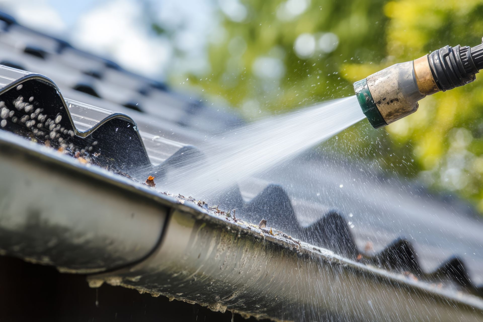 A person is using a hose to clean a gutter on a roof.