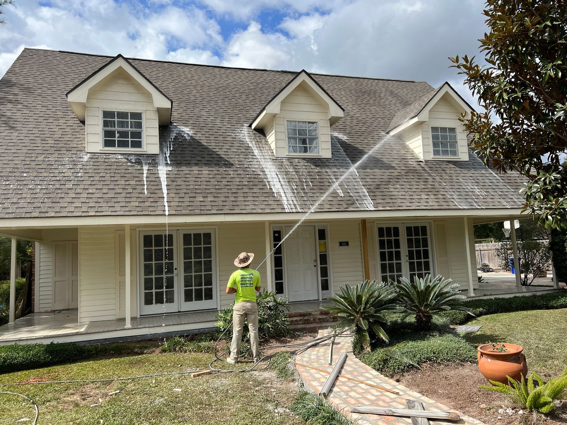 A man is cleaning the roof of a house with a hose.