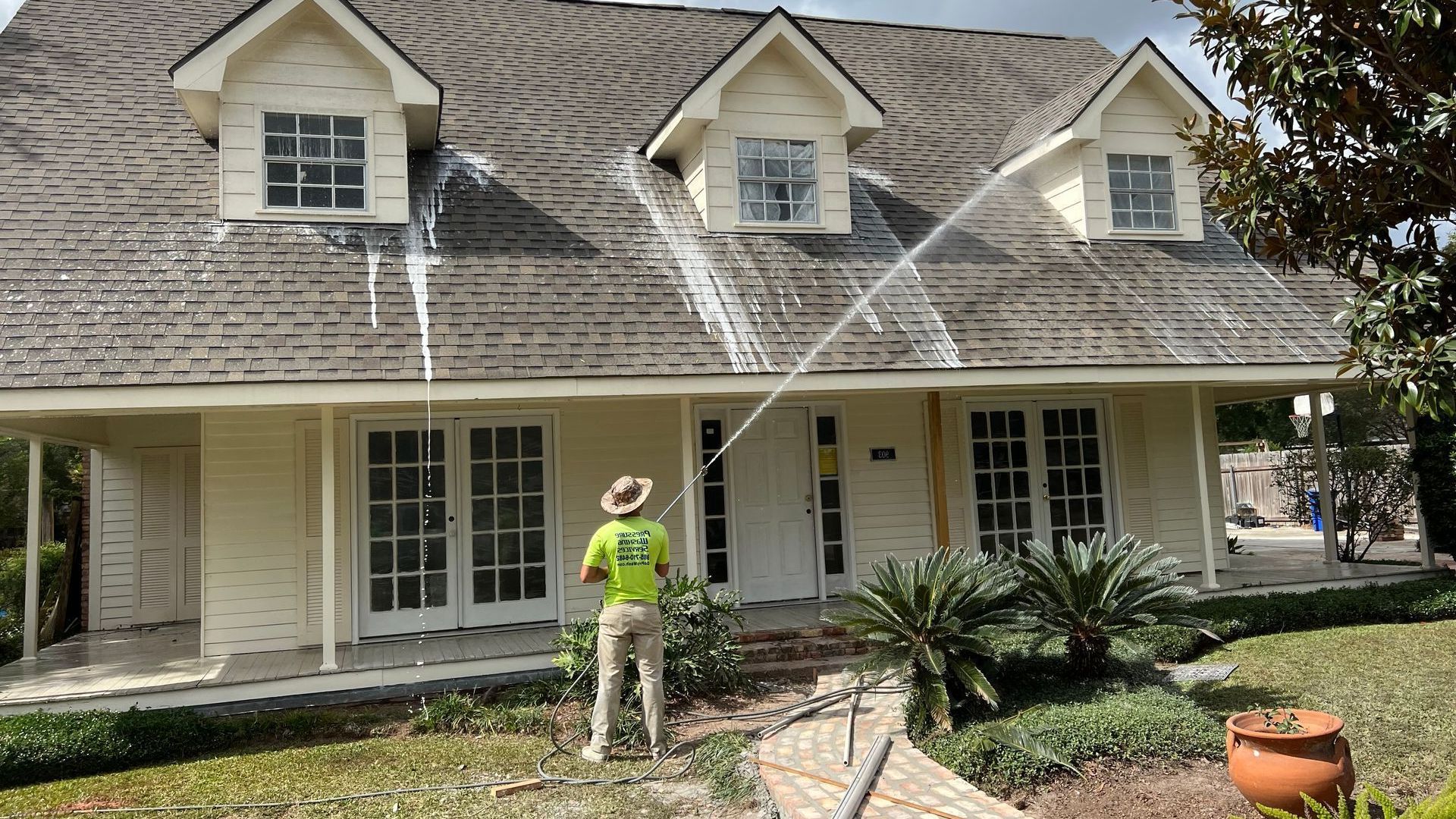 A man is cleaning the roof of a house with a hose.