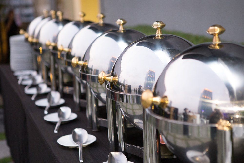 Row of polished silver chafing dishes with gold lids on a buffet table