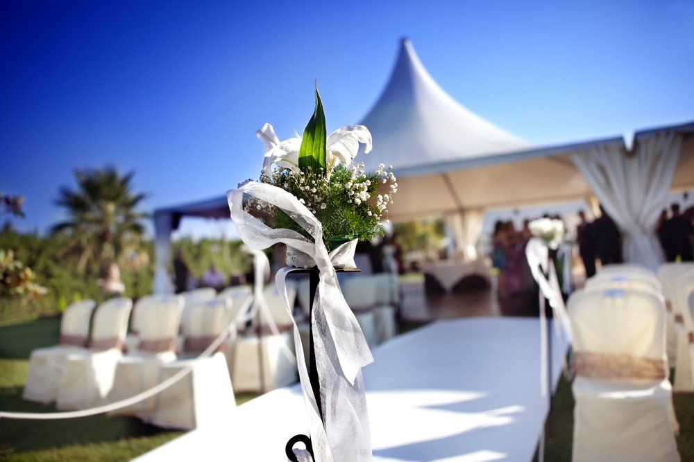 Outdoor wedding reception with white tents, decorated chairs, and a floral aisle centerpiece.