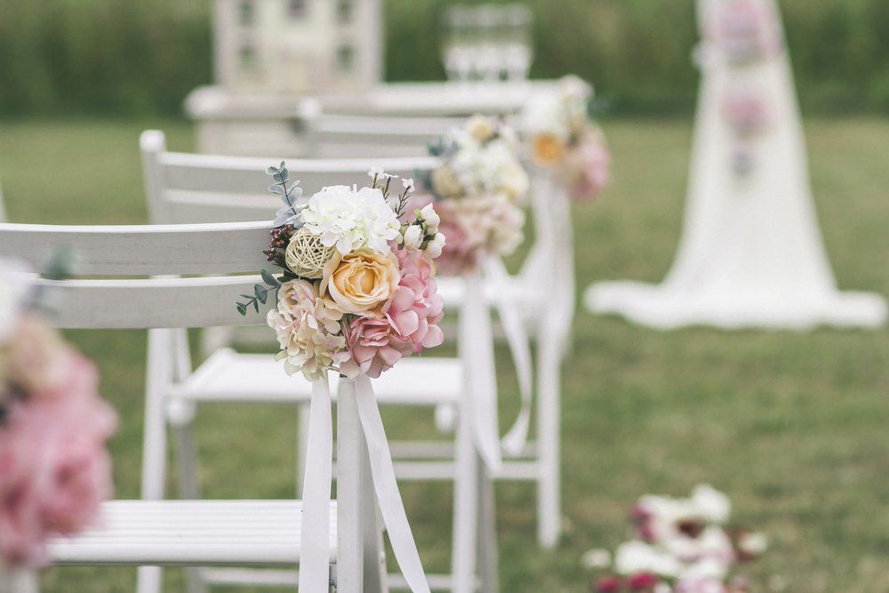 White chairs with pastel floral bouquets arranged on a grassy outdoor wedding aisle