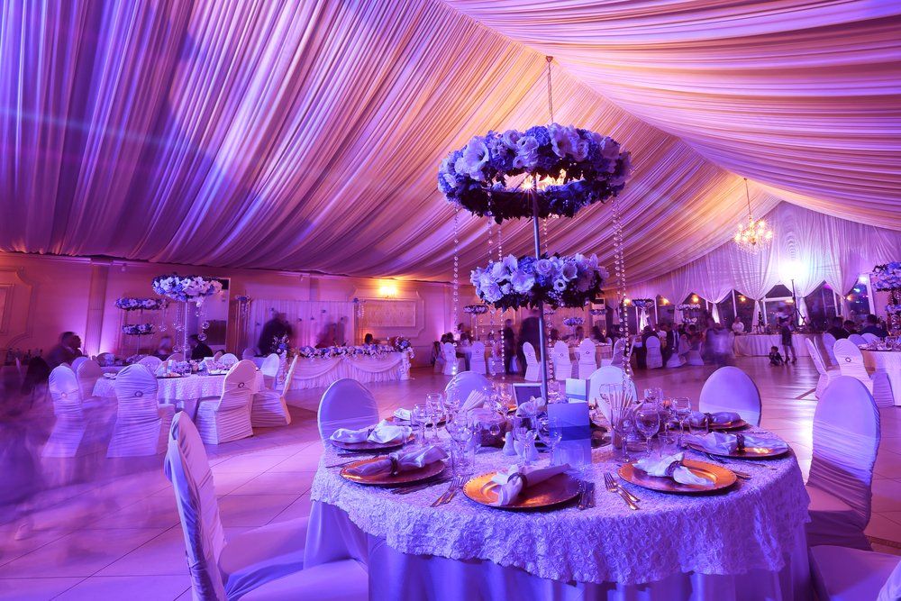 Lavender-lit wedding reception tent with draped ceiling, round tables, and floral centerpieces