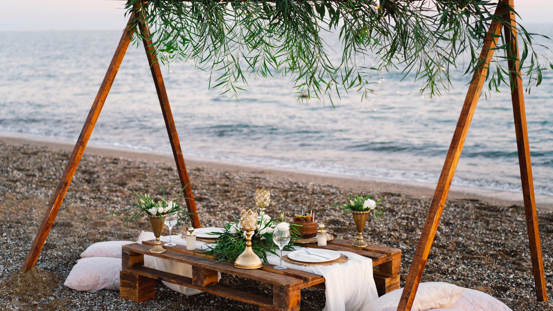 Beach picnic setup with wooden table, decor, and ocean view.