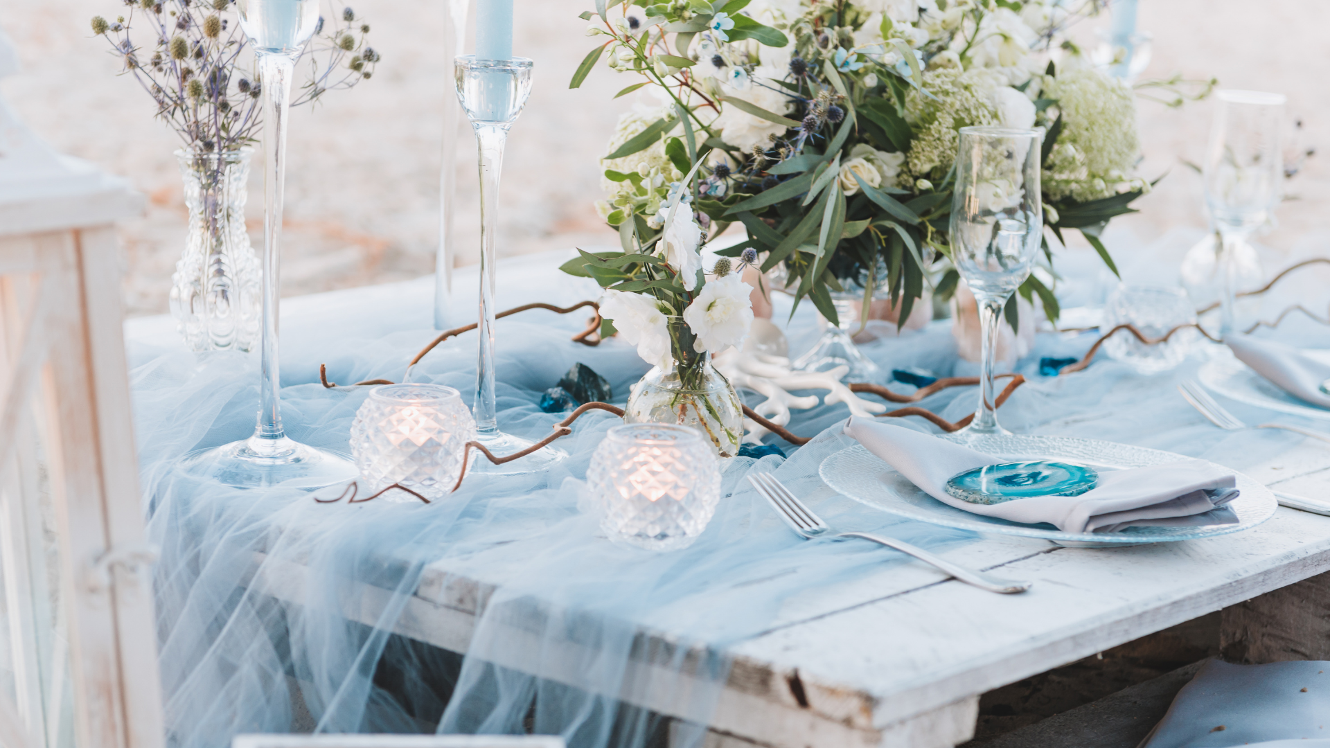 White table set for a wedding with flowers, candles, and blue accents.