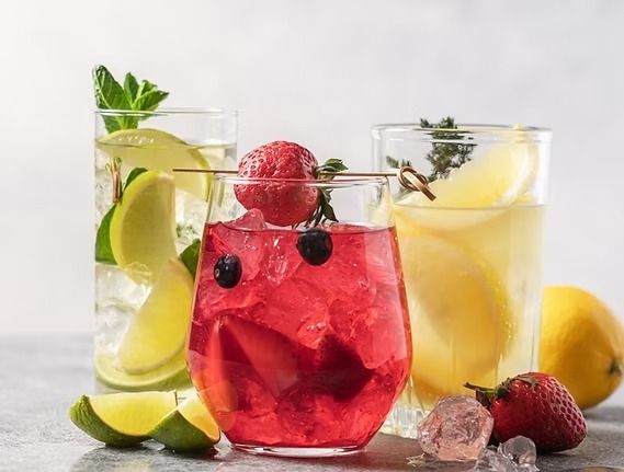 Three colorful cocktails with fruit and ice; a lime, berry, and lemon drink.