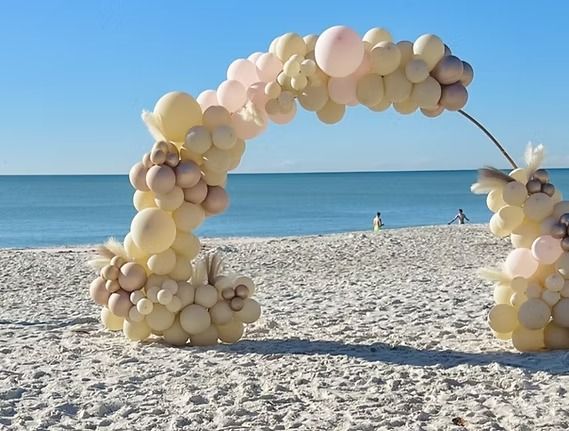 Balloon arch on a sandy beach with the ocean in the background; pastel colors.
