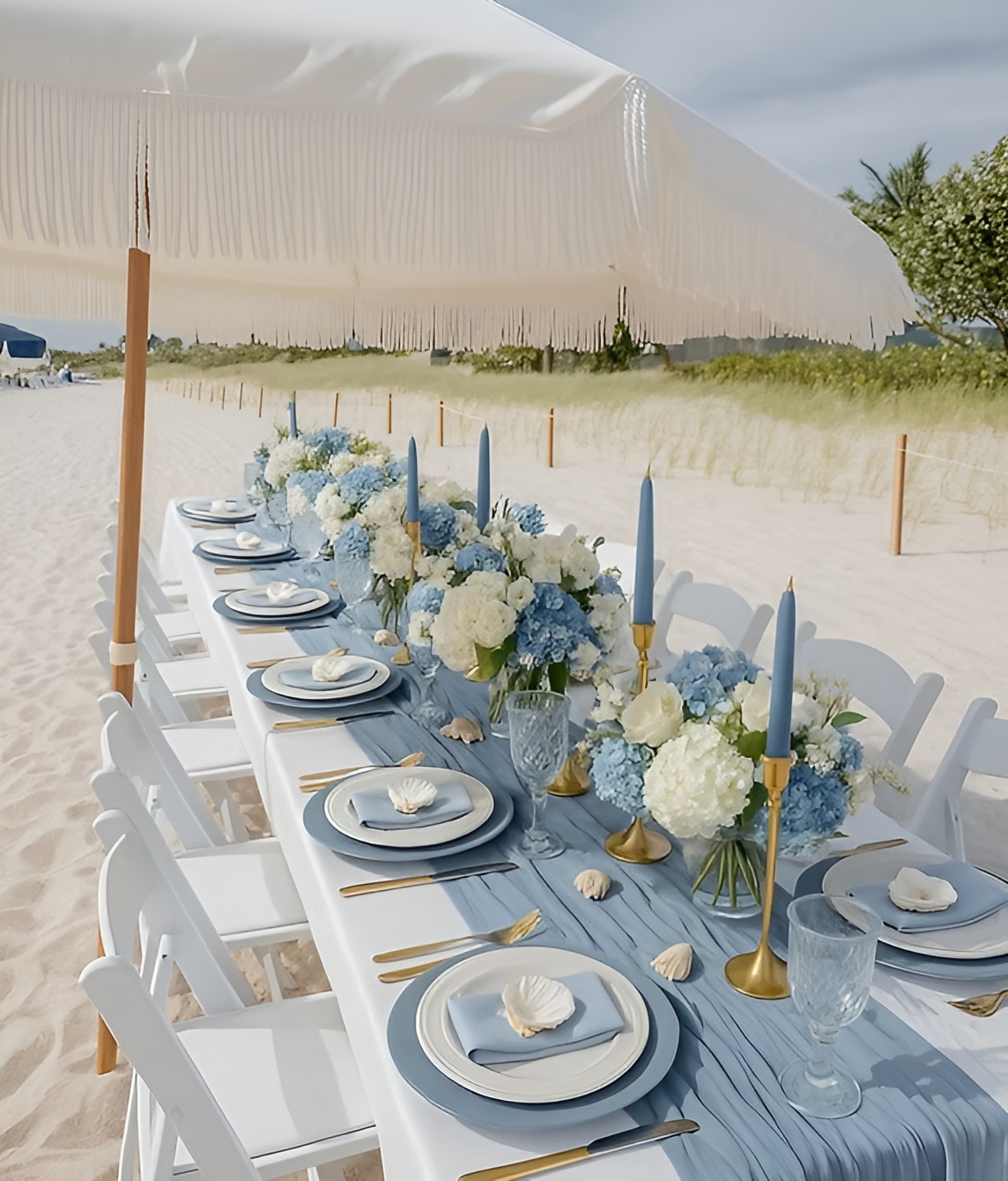 Beachside wedding reception table setting with candles, flowers, and ocean backdrop.
