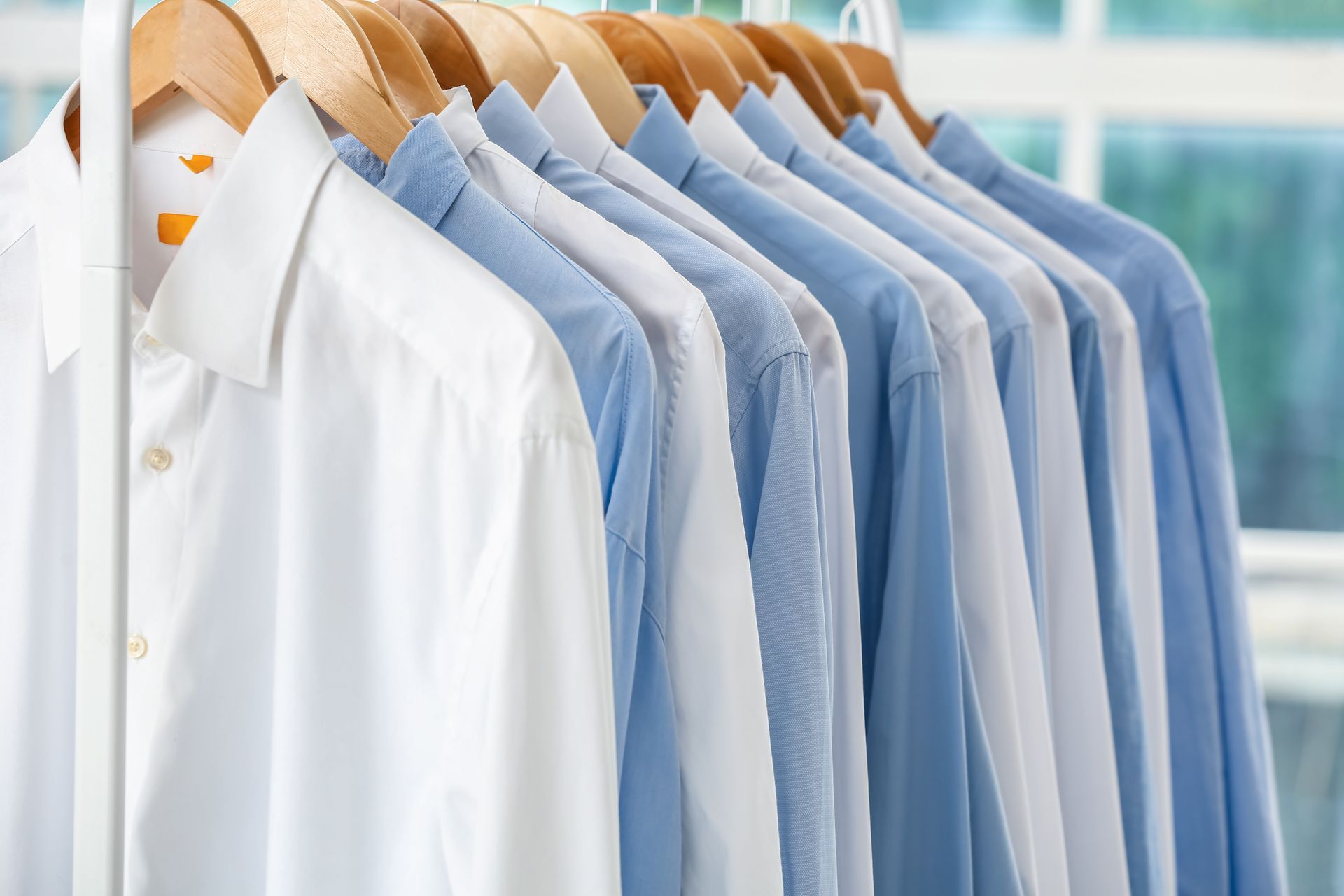 Row of button-down shirts on wooden hangers, varying shades of blue and white, hanging on a metal ra