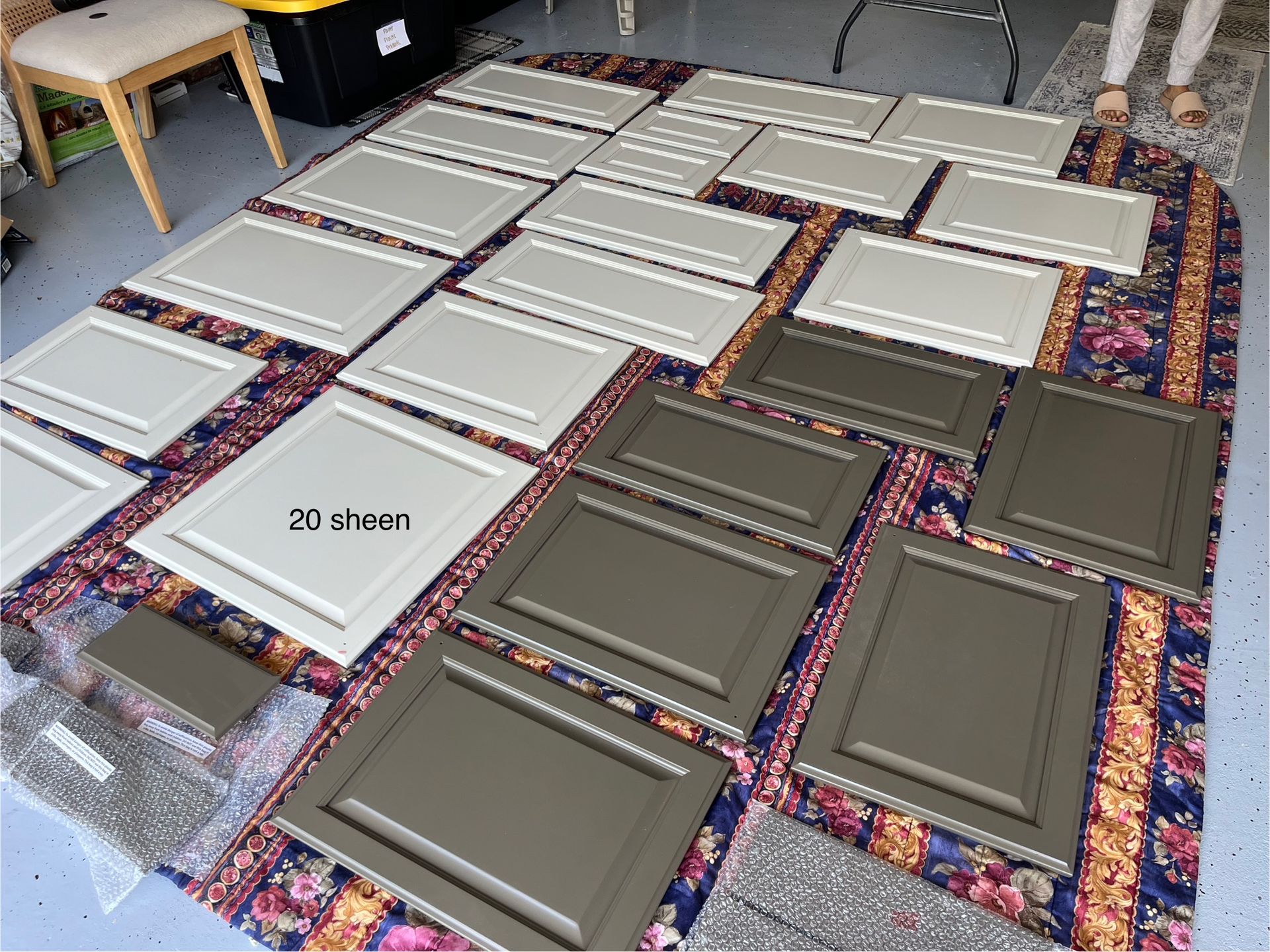 Cabinet doors in light gray and olive green shades laid out on a floral floor covering for painting or refinishing.