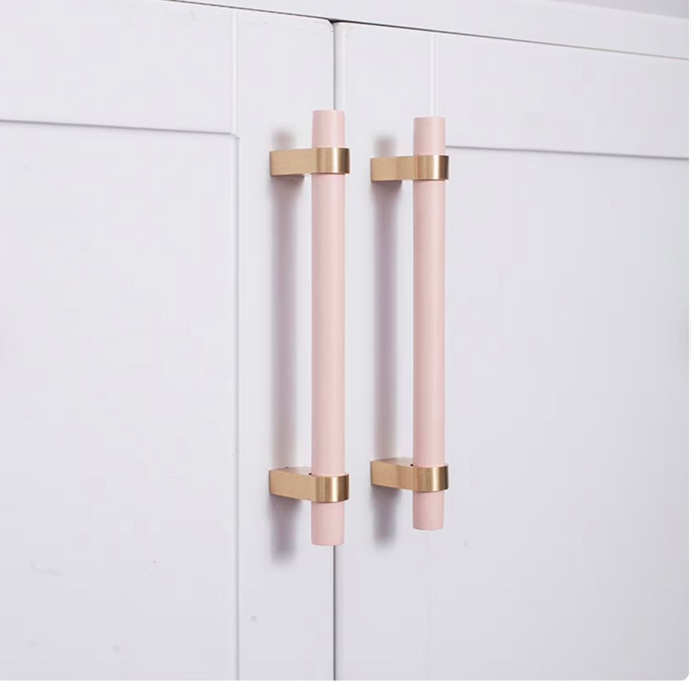 A pair of pink and gold cabinet handles on a white cabinet.