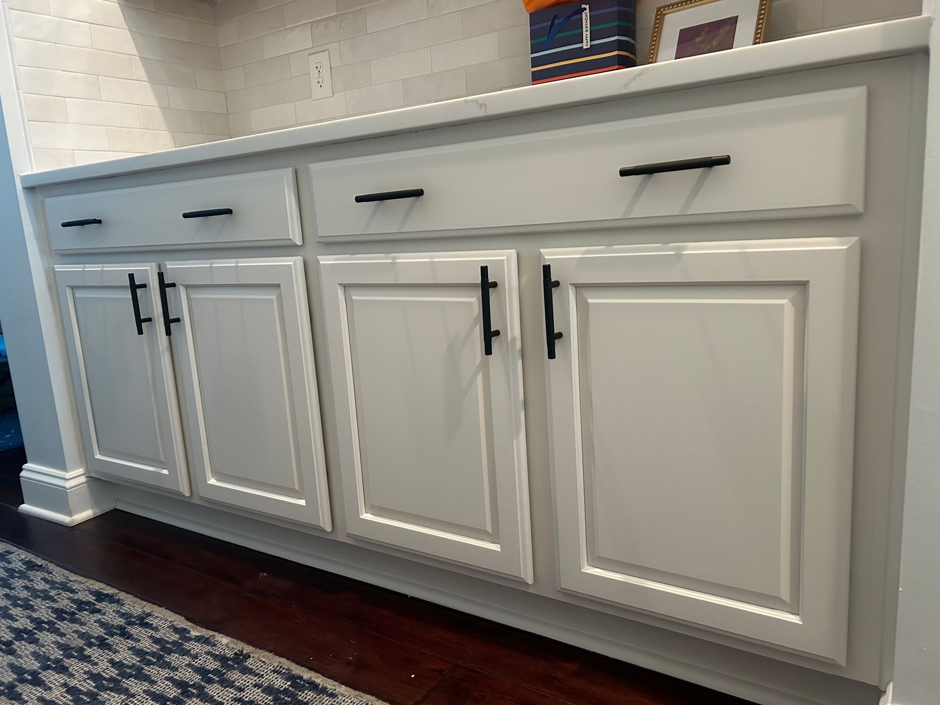 A kitchen with white cabinets and black handles.