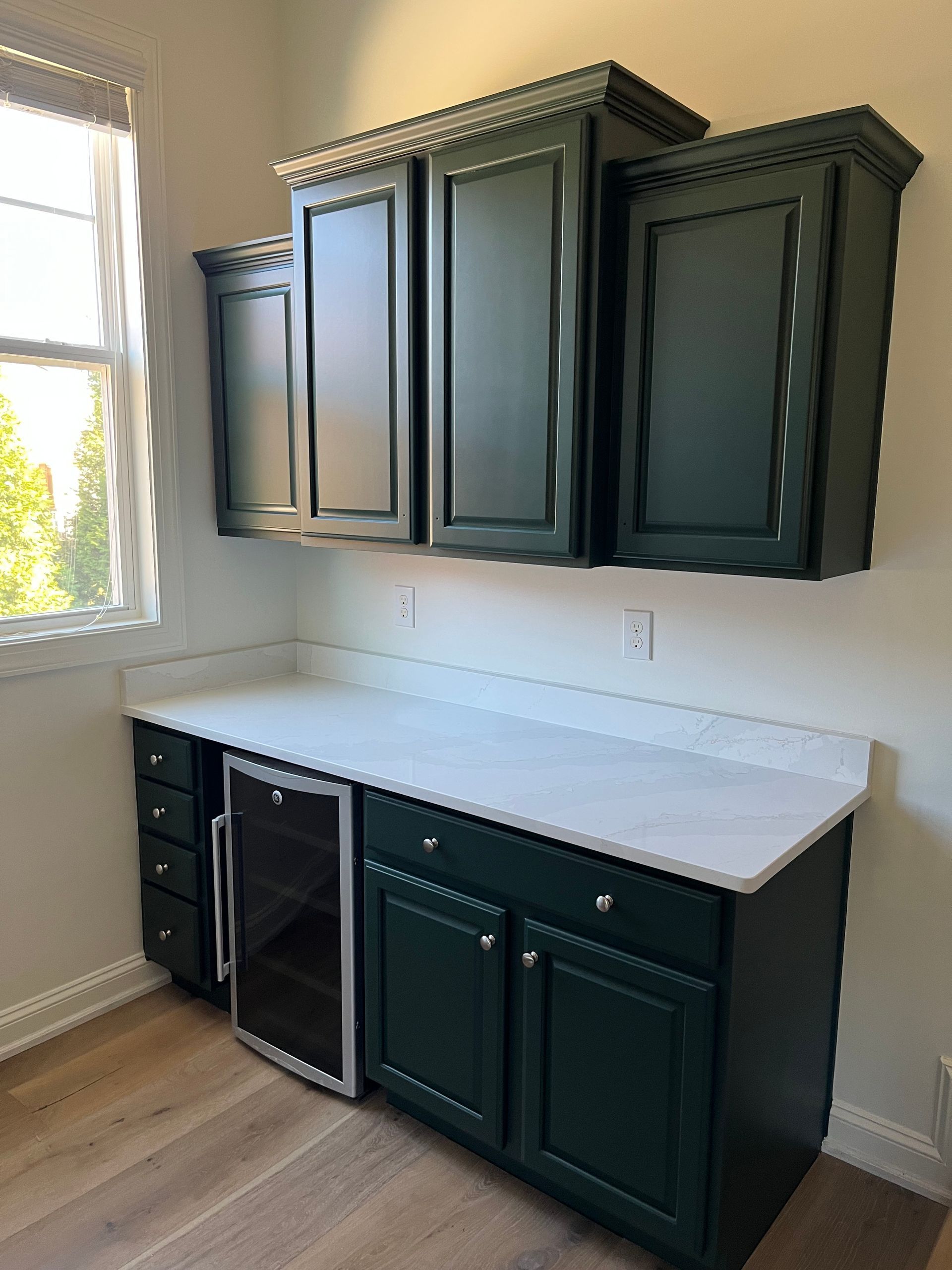 A kitchen with green cabinets and a wine cooler.