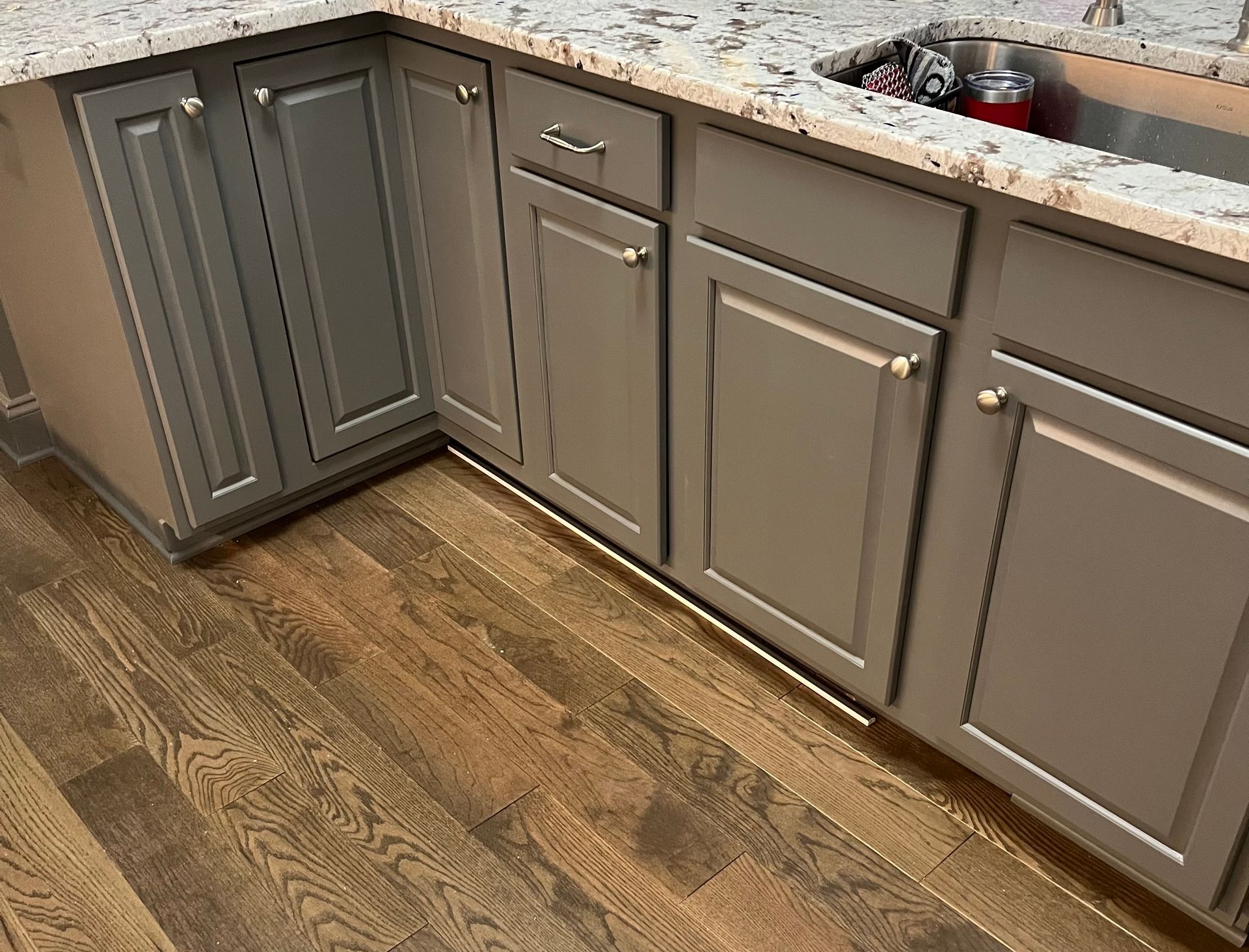 A kitchen with gray cabinets , granite counter tops , and a sink.