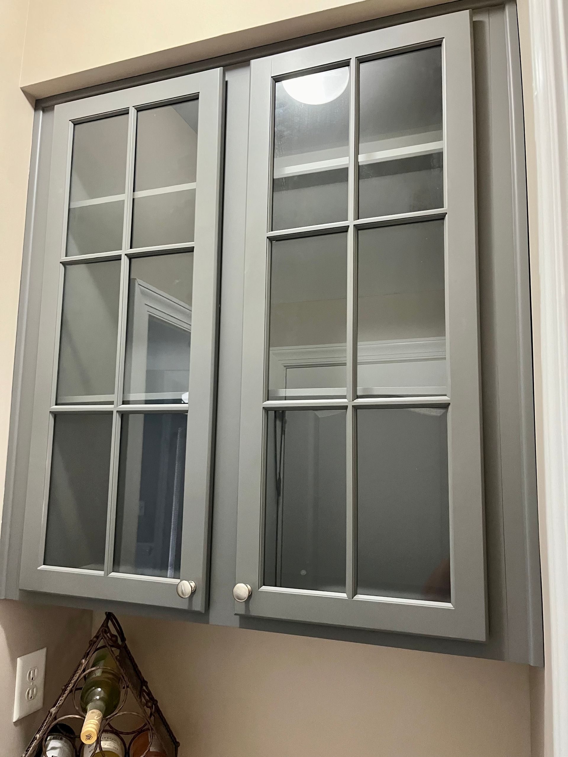 A gray cabinet with glass doors is hanging on a wall.