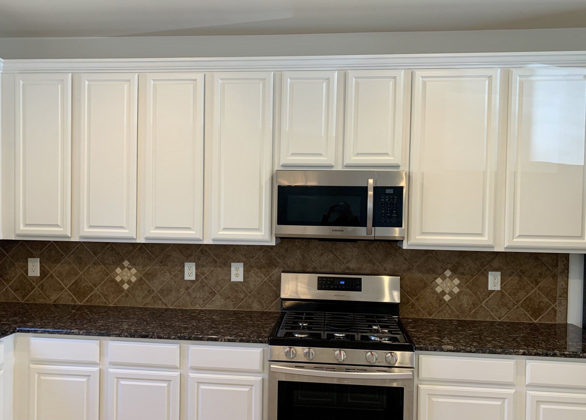 A kitchen with white cabinets , stainless steel appliances , granite counter tops and a stove.