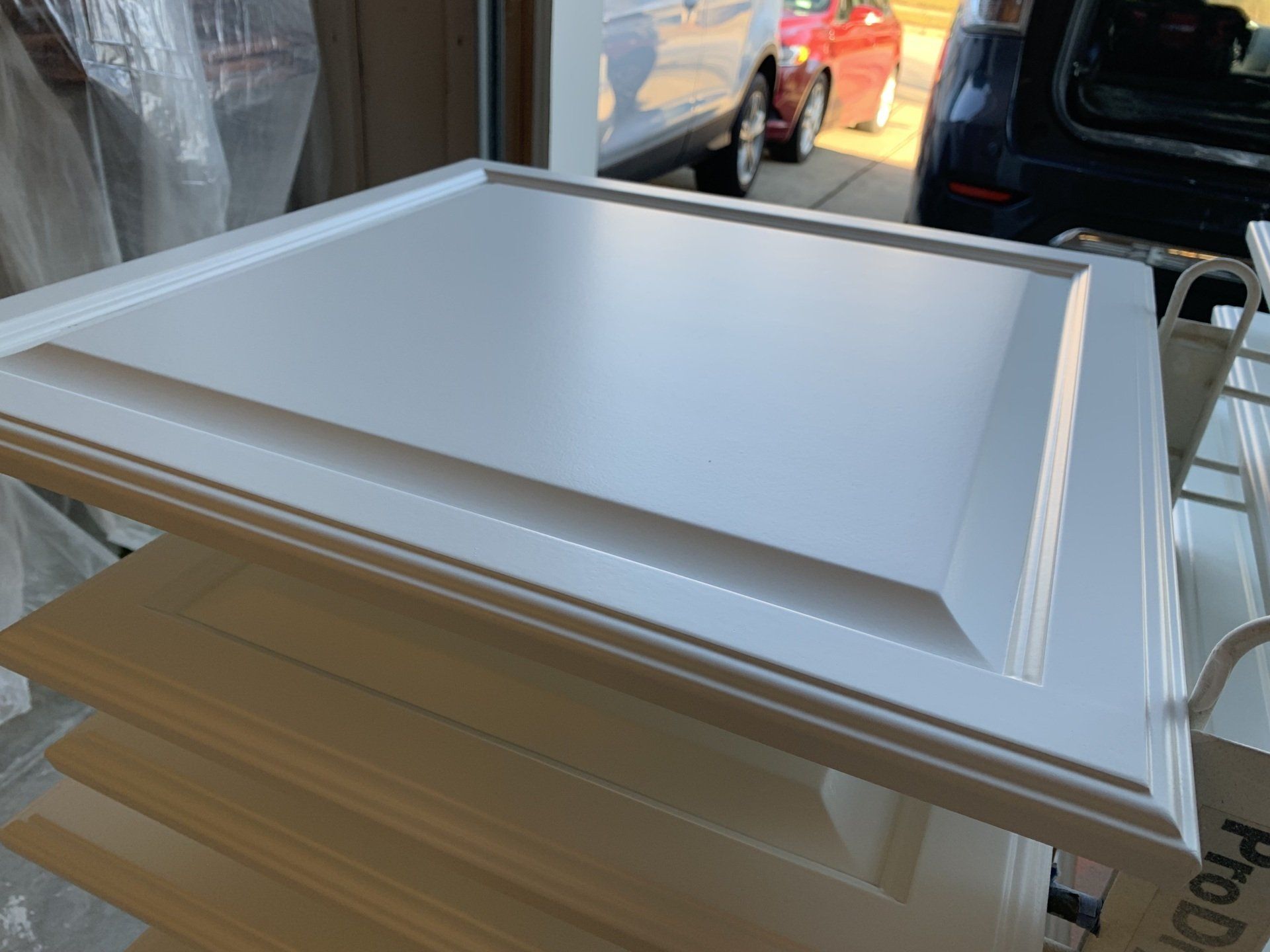A white cabinet door is sitting on top of a wooden shelf in a garage.