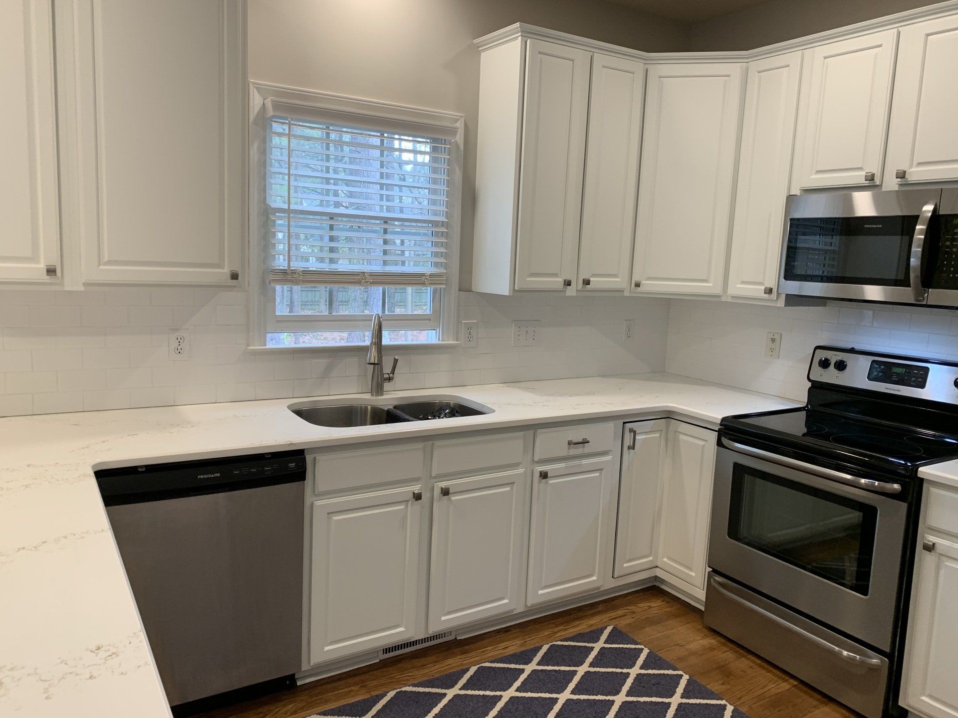 A kitchen with white cabinets , stainless steel appliances , a sink , and a window.