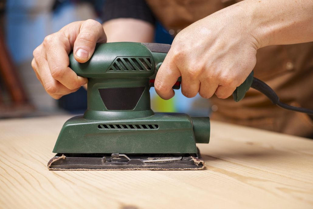 A person is sanding a piece of wood with a sander.