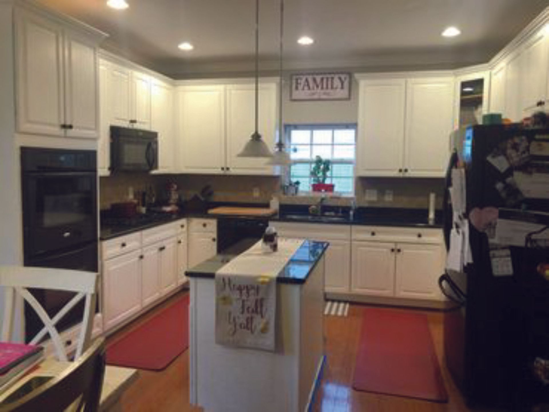 A kitchen with white cabinets , black counter tops , a refrigerator and a sign that says `` family ''.