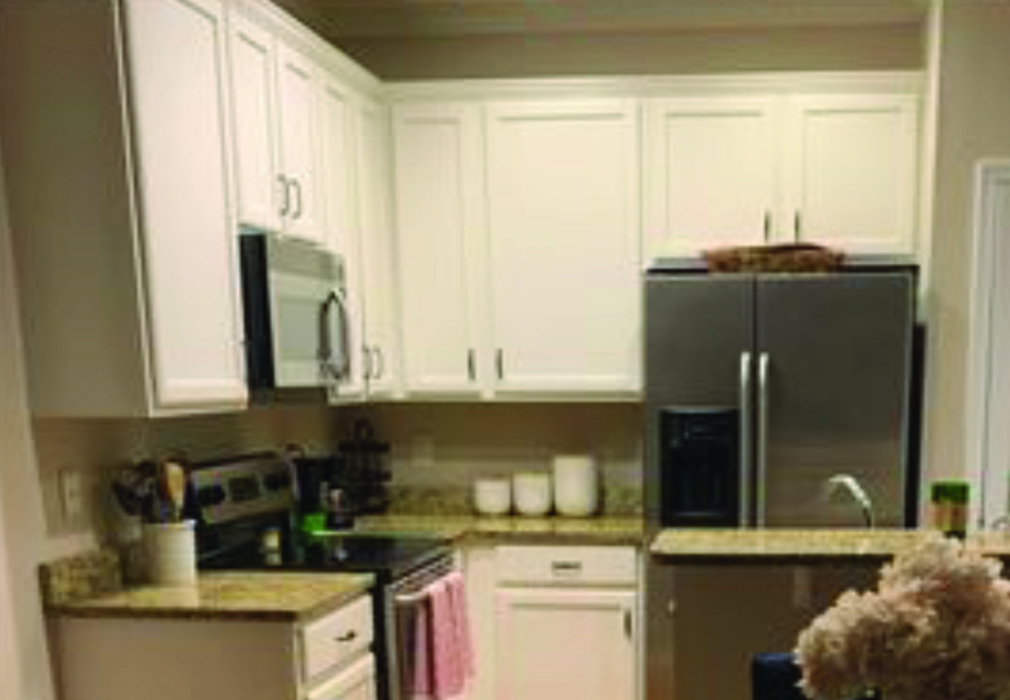 A kitchen with white cabinets , stainless steel appliances , a refrigerator and a sink.