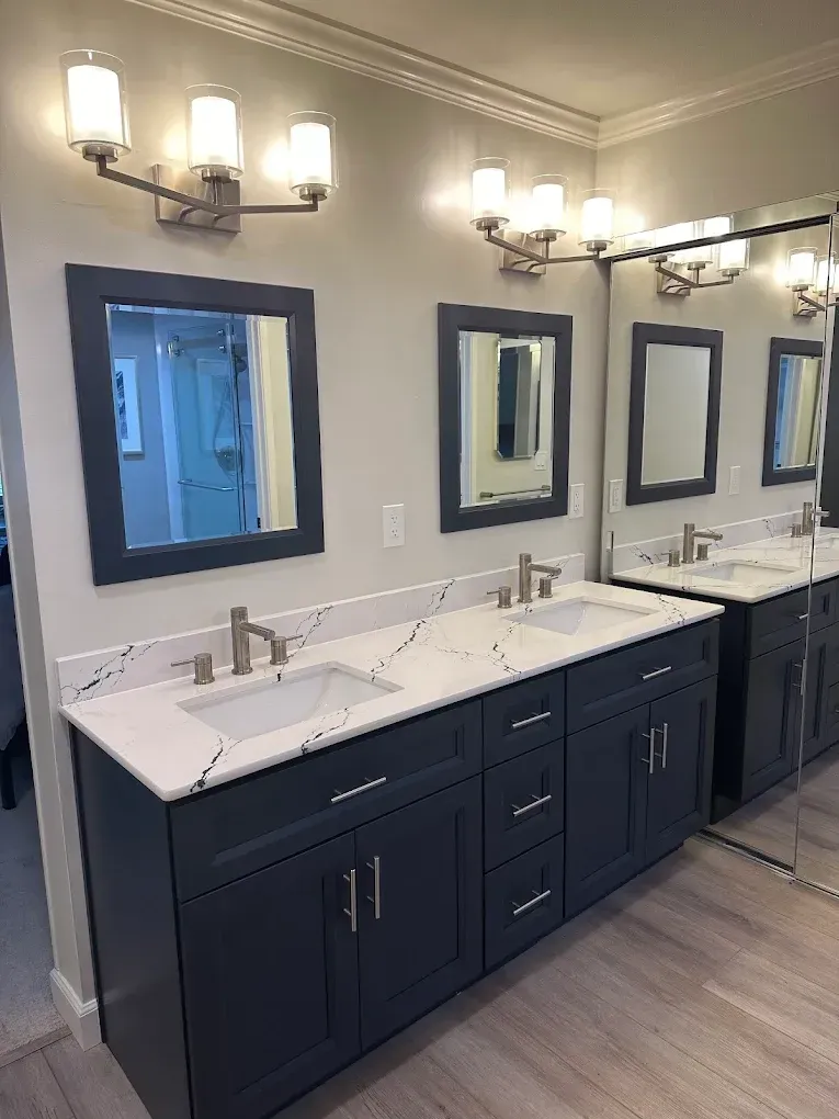 Modern bathroom with navy double vanity, white sinks, large mirrors, and wall sconces