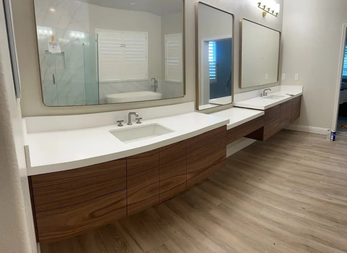 Modern bathroom vanity with long white countertops, mirrors, sinks, and wood cabinets in a bright interior.
