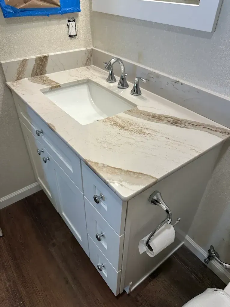 Bathroom vanity with white marble countertop, sink, mirror, and mounted toilet paper holder.
