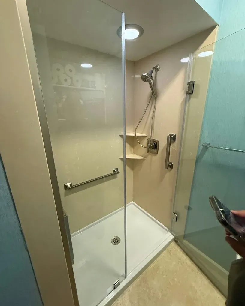 Small beige bathroom with a glass shower stall, handheld showerhead, and white shower base.