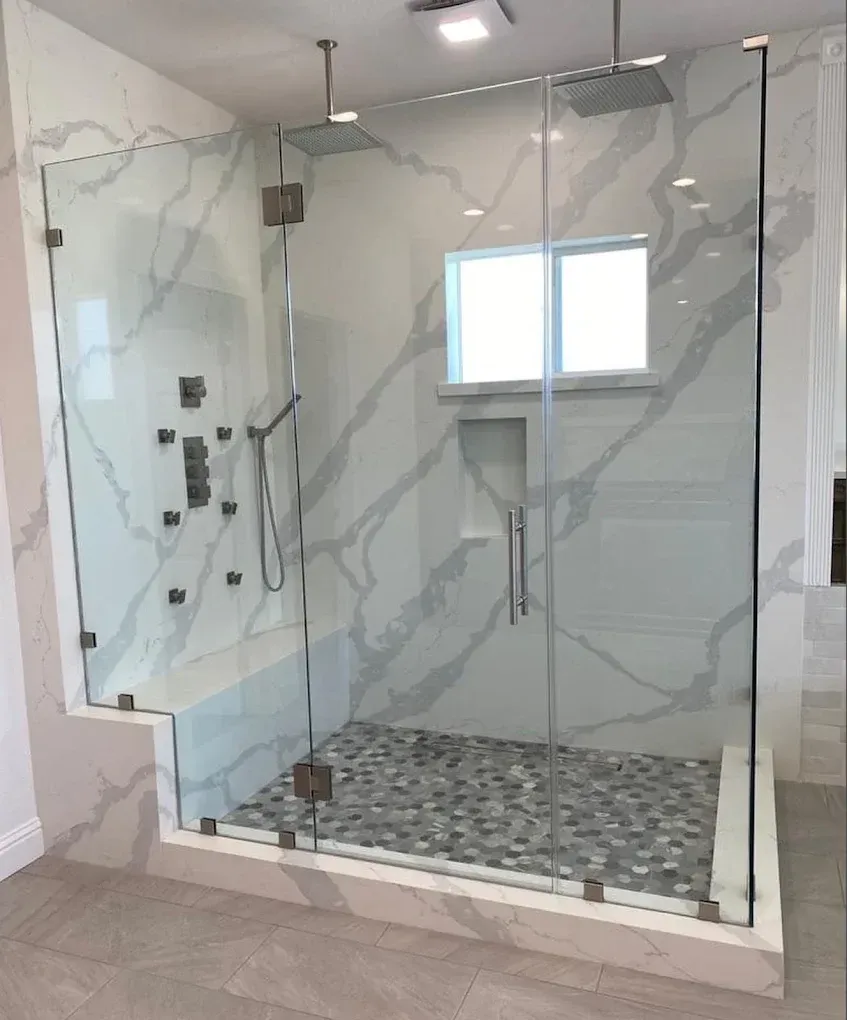 Modern glass walk-in shower with marble walls, gray mosaic floor, and a window.