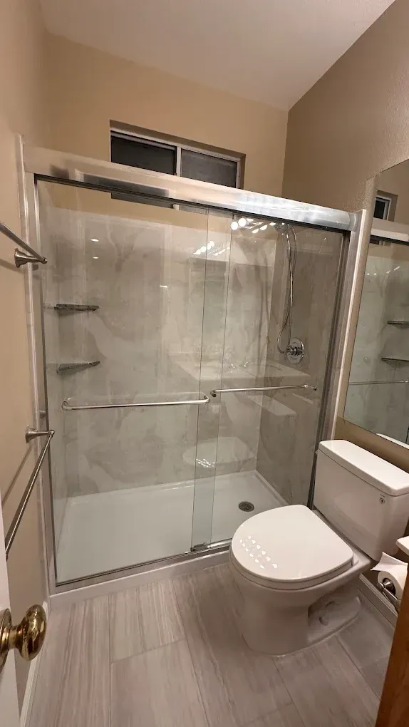 Small bathroom with glass-enclosed shower, toilet, and beige tile walls.