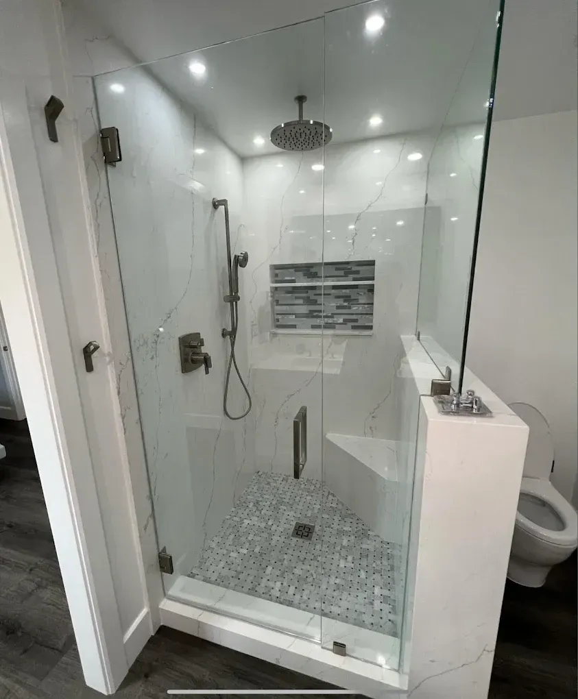 Glass walk-in shower with rainfall showerhead and pebble tile floor in a white bathroom