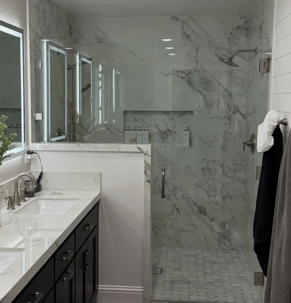 Modern bathroom with glass shower, marble-look tile, and vanity with sink and mirror