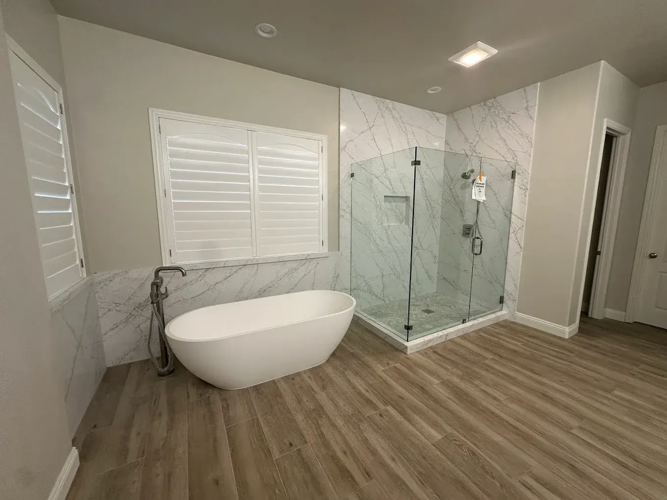 Modern bathroom with freestanding tub, glass shower, marble walls, and wood-look flooring