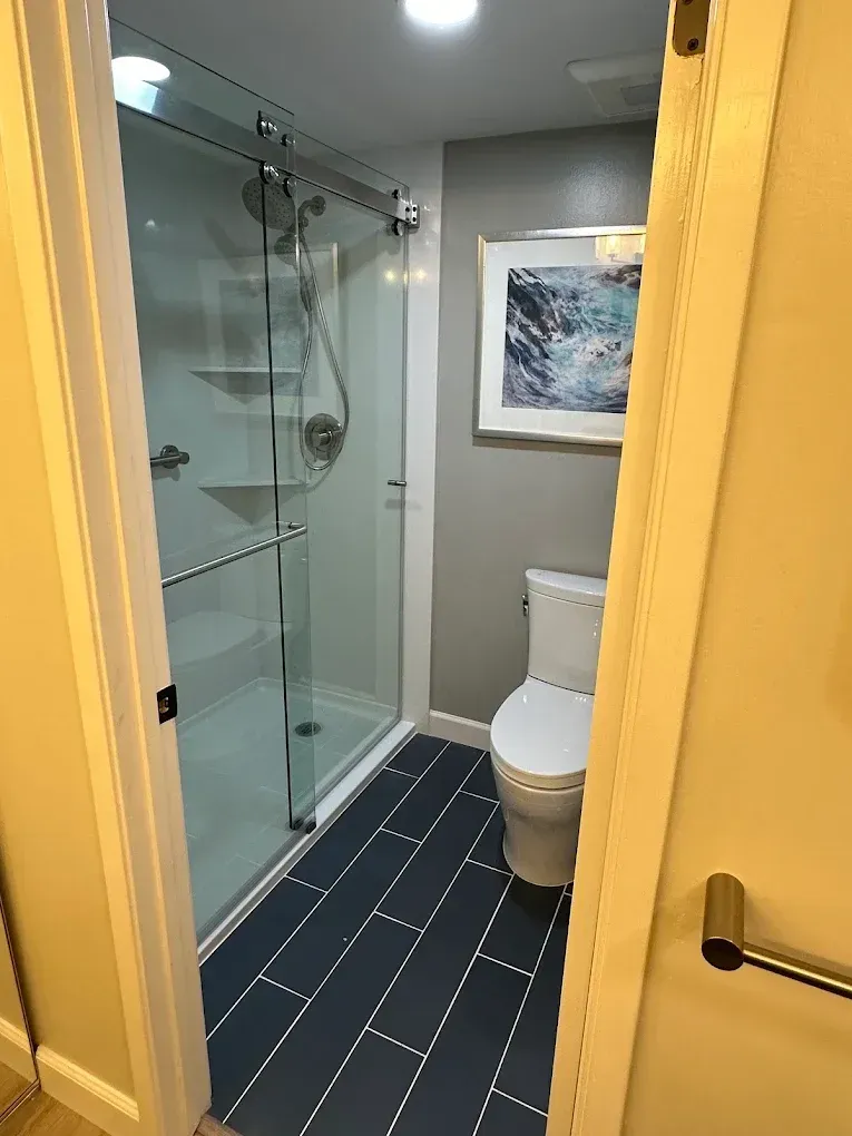 Small modern bathroom with glass shower, toilet, gray walls, and blue floor tiles.