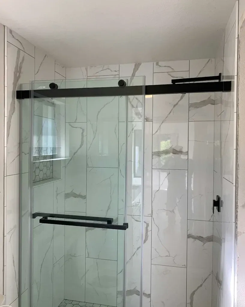 Glass shower enclosure with black hardware in a tiled bathroom