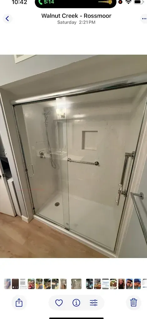 White walk-in shower with glass doors, chrome grab bars, and a built-in bench in a bathroom
