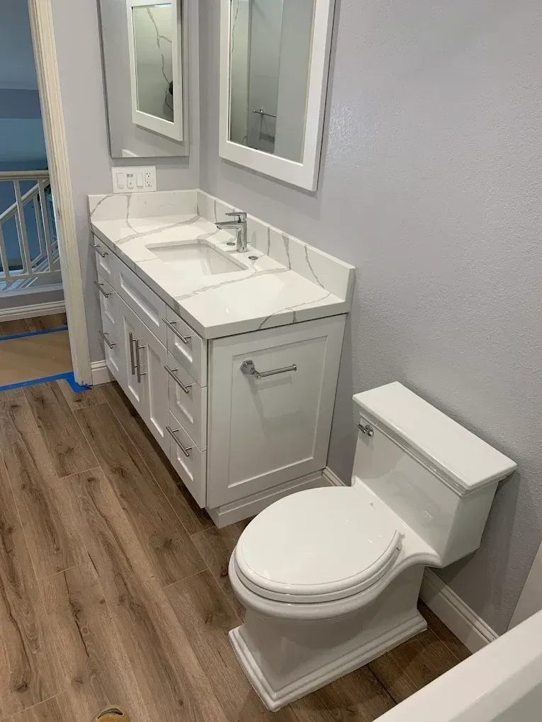 White bathroom vanity and toilet in a small room with gray walls and wood-look flooring.