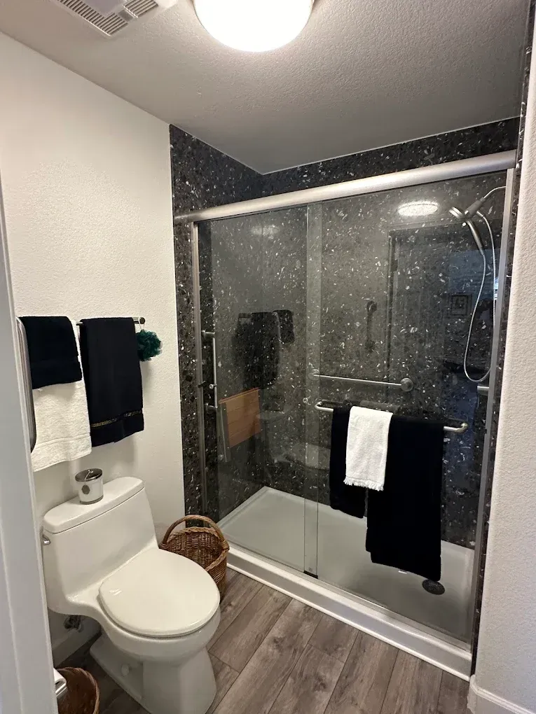 Modern bathroom with glass shower, toilet, and dark towels on a towel rack.