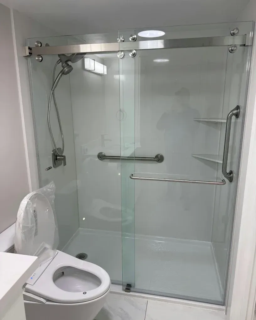 Accessible bathroom with a toilet and glass shower enclosure, including grab bars and a fold-down seat