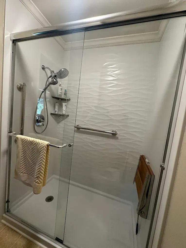 Glass shower stall with chrome fixtures and a beige towel hanging inside.