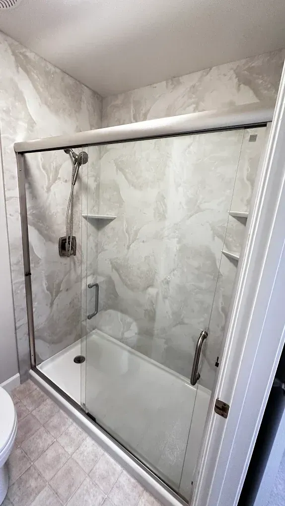 Glass shower enclosure with marble-look walls and a handheld showerhead in a bathroom