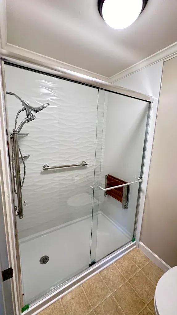 Glass-enclosed shower with chrome fixtures, white tile walls, and tan bathroom floor tile