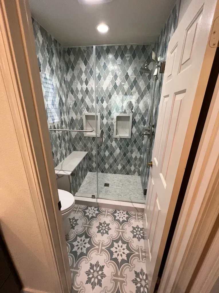 Small bathroom with patterned tile floor, walk-in shower, and wall-mounted toilet.