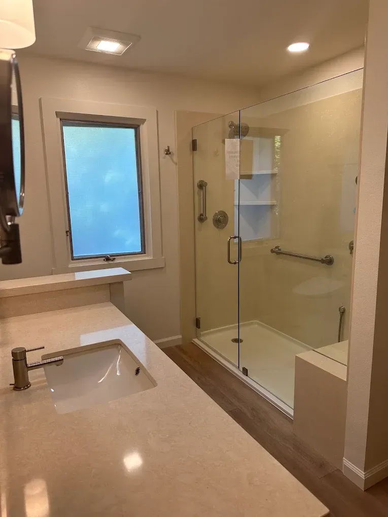 Modern bathroom with glass shower, vanity sink, beige tile, and frosted window