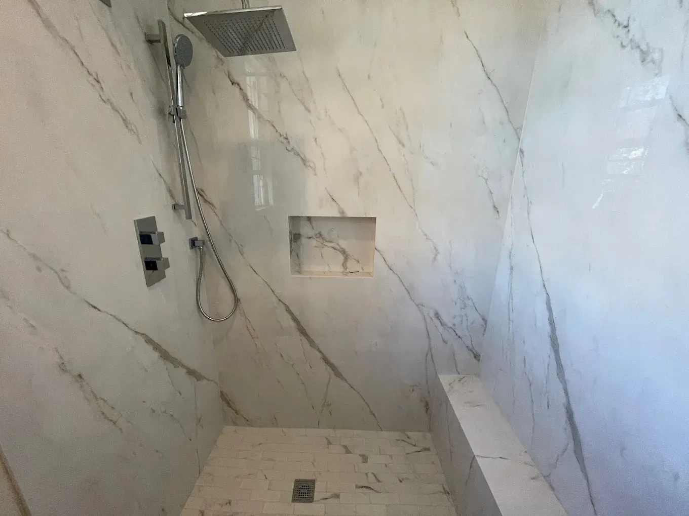 Empty tiled shower with gray marble-pattern walls, a recessed niche, and a handheld showerhead.