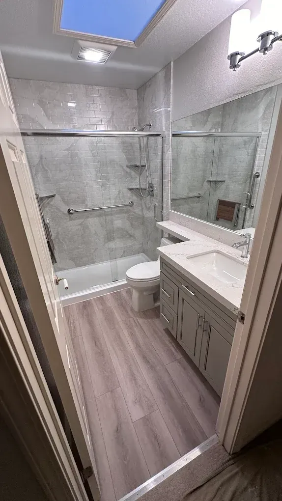Small modern bathroom with glass shower, vanity, toilet, and skylight, in gray tones